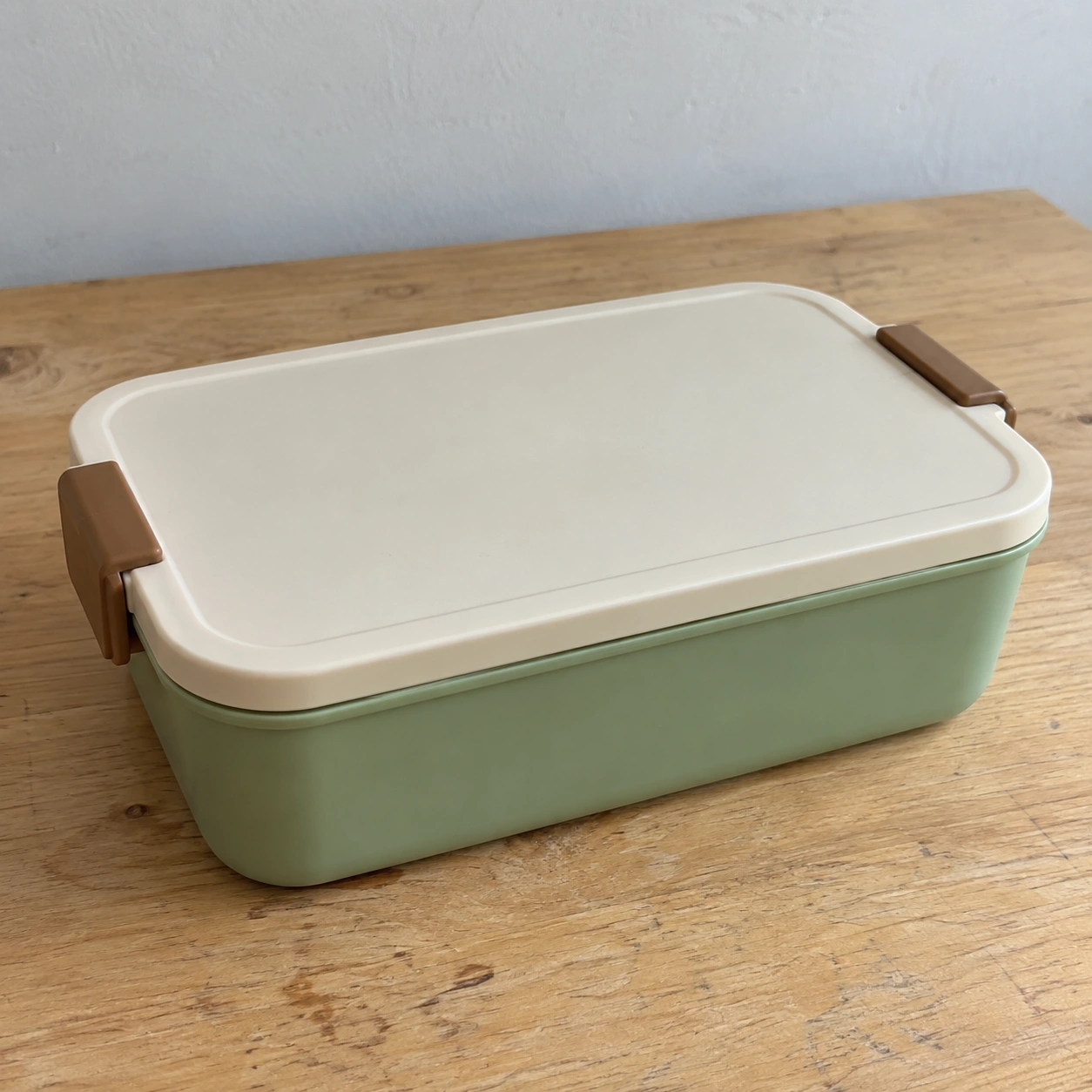 Lunch-box teaching source with a green body, cream lid and two brown side clasps on a wooden table